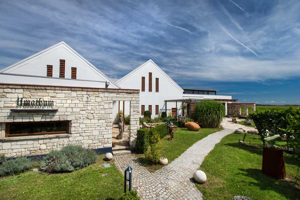 Weingut Umathum: weiße Gebäude mit Steinmauer und Garten unter blauem Himmel