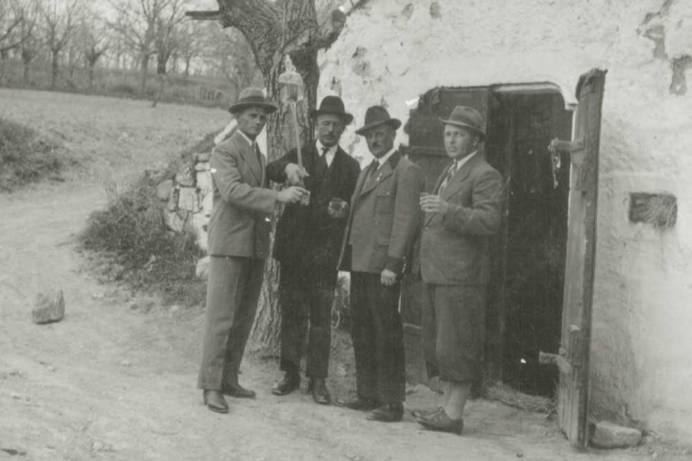 Historisches Schwarz-Weiß-Foto: vier Männer mit Weingläsern vor einem Weinkeller